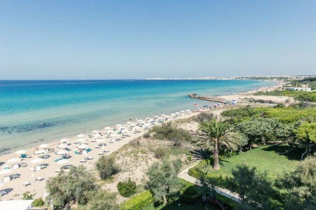 Una spiaggia con ombrelloni e lettini su sabbia dorata, mare blu e cielo limpido.