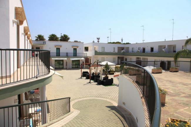 Vista dall'alto di un cortile collegato da una rampa curvilinea, con sedute e piante al centro.