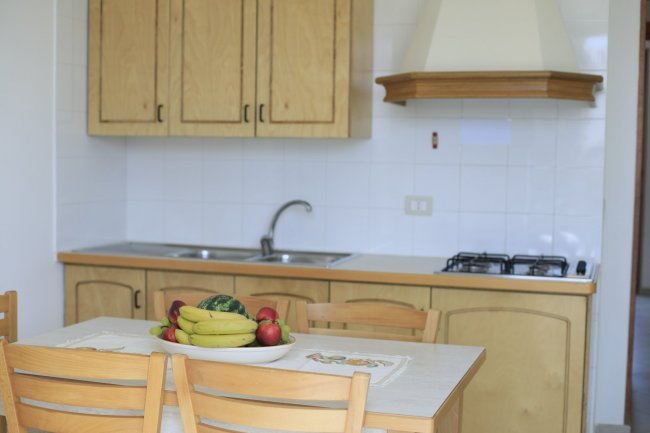 Cucina con mobili in legno chiaro, tavolo da pranzo e frutta fresca in esposizione.