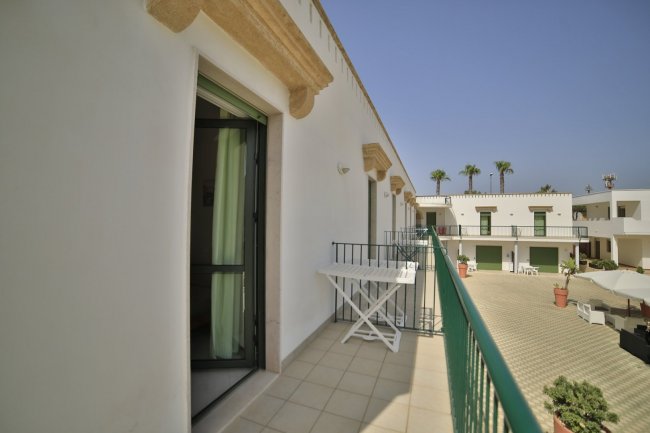 Balcone con un parapetto verde, vista su un cortile con palme e edifici intorno.