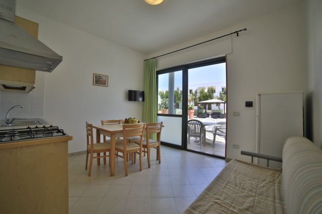 Una sala con cucina aperta, tavolo da pranzo, divano e una finestra che dà su un balcone.