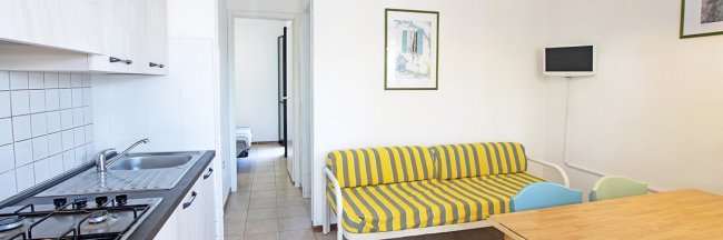 Soggiorno con cucina, divano a righe e TV a muro.