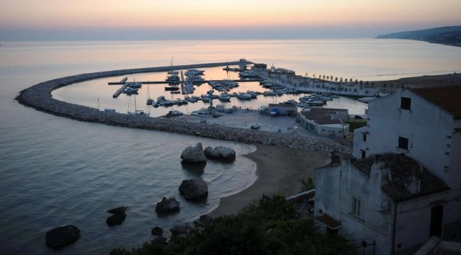 Porto al tramonto con barche ormeggiate e scogli.