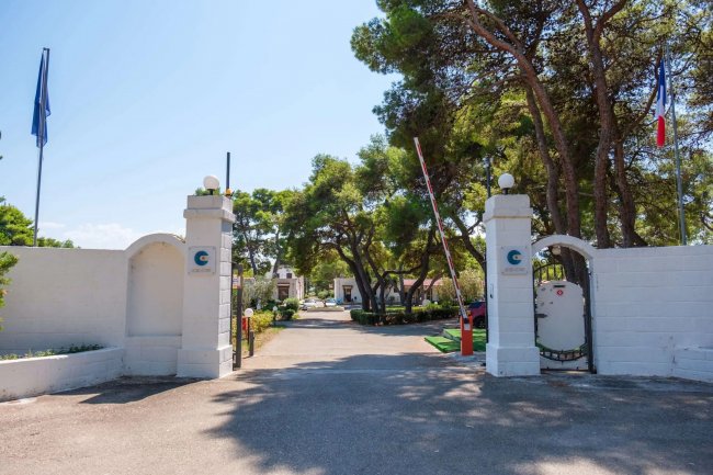 Ingresso con cancelli bianchi e alberi sullo sfondo.