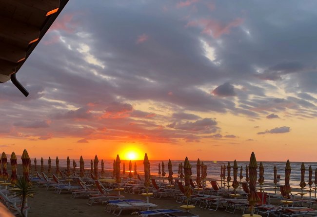 Tramonto su una spiaggia con ombrelloni chiusi.