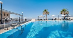 Piscina con due palme e ombrelloni, vista mare e cielo sereno.