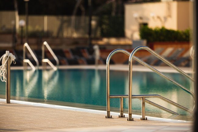 Una piscina con scale metalliche e lettini sul bordo.