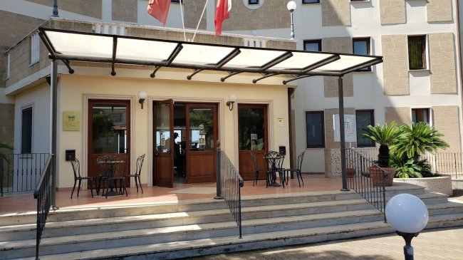 Entrata di un edificio con gradini, sedie esterne e due bandiere sopra.
