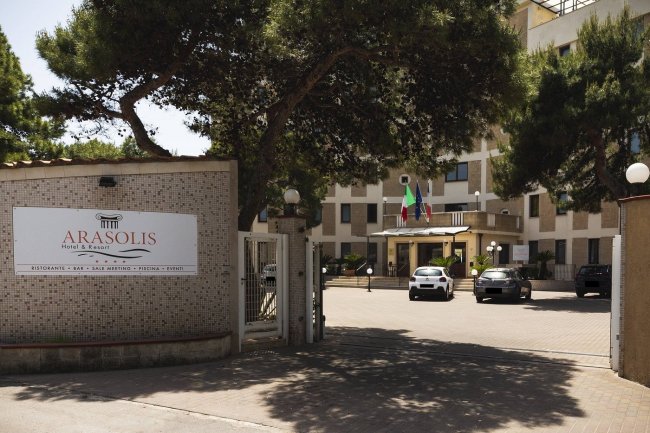 Ingresso di un hotel con segnaletica, auto parcheggiate e bandiere.