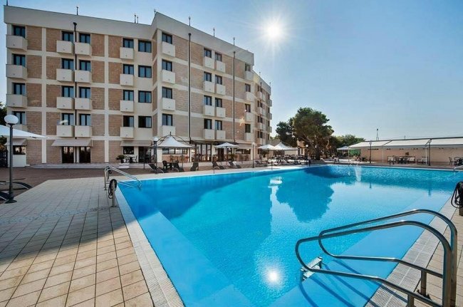 Piscina all'aperto davanti a un edificio a più piani sotto il sole.
