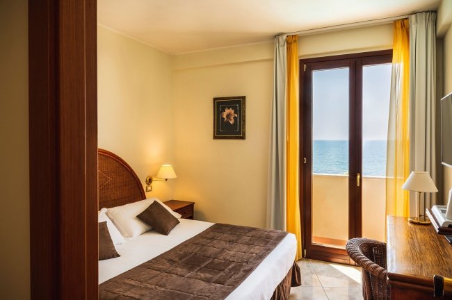 Camera da letto luminosa con vista mare, letto matrimoniale e mobili in legno.