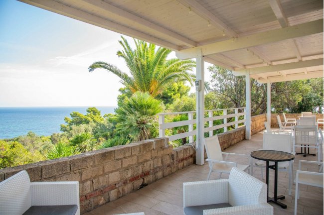 Terrazza coperta con vista sul mare e vegetazione rigogliosa.