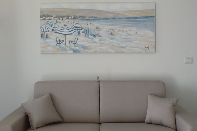 Divano beige con quadro di una spiaggia sopra.