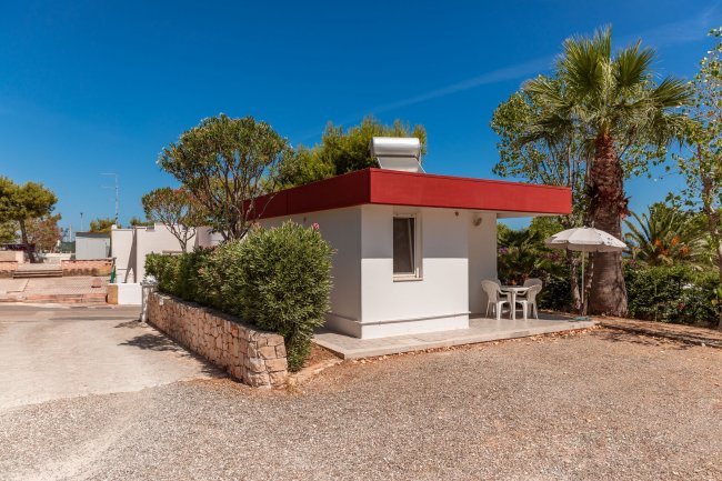 Piccola casa bianca con tetto rosso e mobili da giardino.