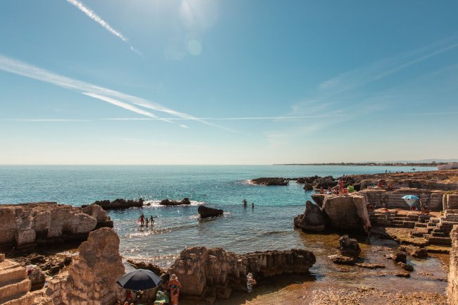 Spiaggia rocciosa con bagnanti e ombrelloni.