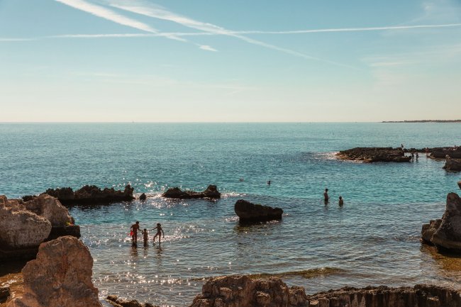 Persone in mare vicino a scogli, cielo limpido.