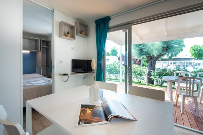 Tavolo bianco, rivista, TV e porta-finestra su veranda.