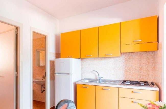 Cucinino arancione con frigorifero e piano cottura.