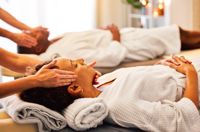 Due persone ricevono un massaggio al viso su lettini da spa.