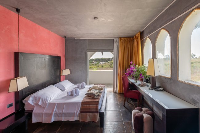 Camera d'albergo con letto, luce naturale e fiori sulla scrivania.