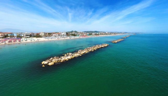 Spiaggia con acque turchesi e barriera frangiflutti.