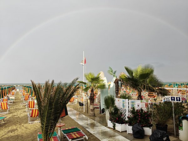 Spiaggia con ombrelloni, palme e arcobaleno.