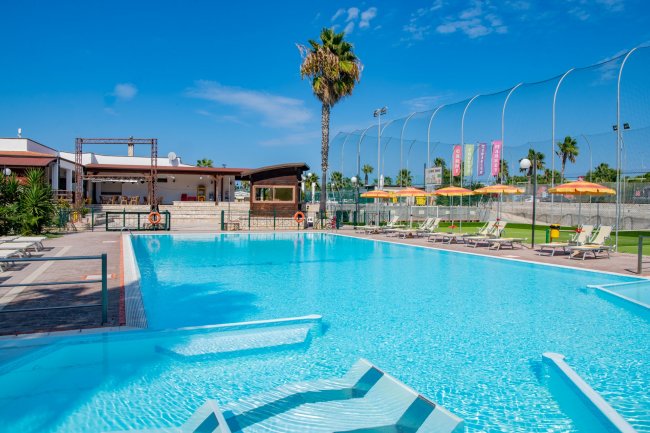 Piscina azzurra, sdraio e ombrelloni, cielo sereno.