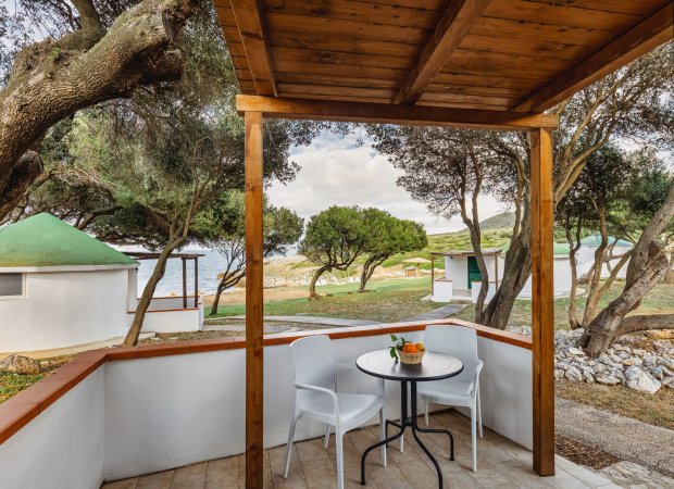 Veranda con tavolo e sedie, vista mare e alberi.