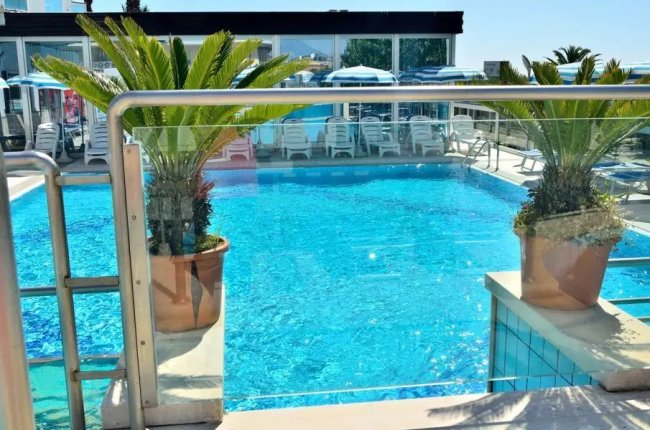 Piscina con piante in vaso e lettini sullo sfondo.