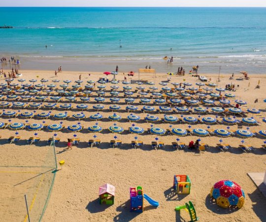 Spiaggia affollata con ombrelloni e giochi per bambini.