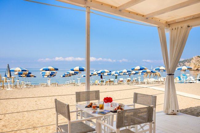 Tavolo con colazione in spiaggia, ombrelloni blu.