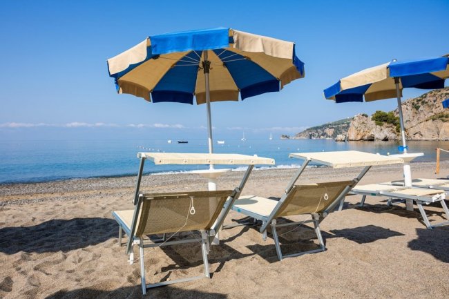Due lettini e ombrelloni blu su una spiaggia sabbiosa.