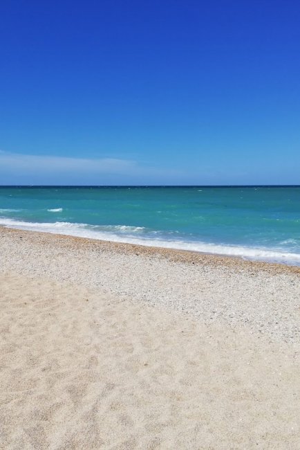 Spiaggia sabbiosa con mare turchese e cielo blu.