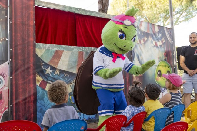 Una mascotte di tartaruga verde interagisce con i bambini seduti.