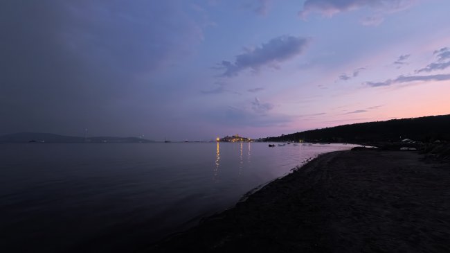 Tramonto su una spiaggia con luci in lontananza.