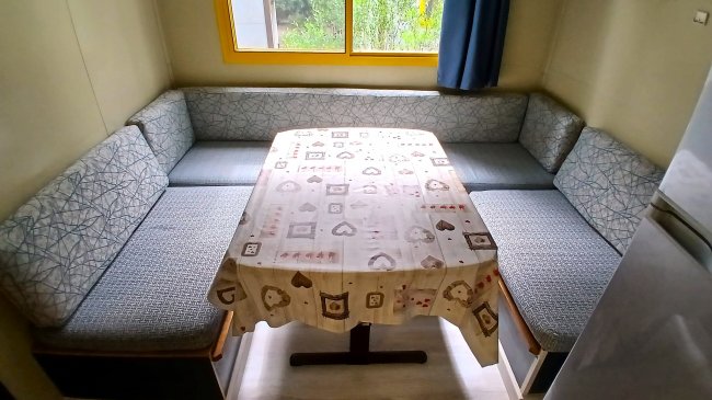 Un angolo pranzo con divani ad angolo, tavolo con tovaglia decorata, accanto a una finestra.