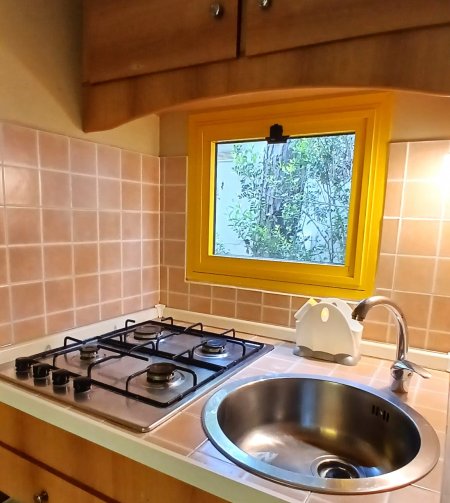 Cucina con piano cottura a gas, lavandino circolare, piastrelle rosa e piccola finestra gialla.