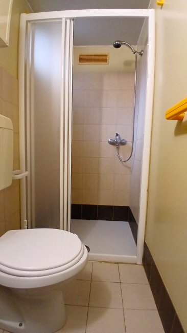 Bagno con doccia, WC e piastrelle chiare; la porta della doccia è scorrevole.