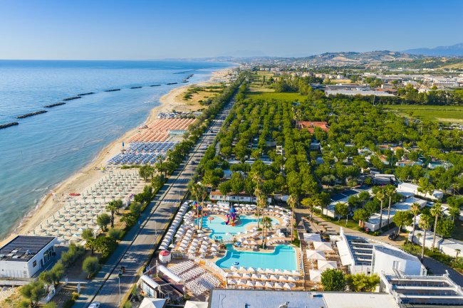 Vista aerea di una spiaggia e piscina con ombrelloni.