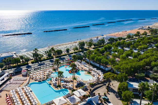 Piscina e spiaggia con mare cristallino dall'alto.