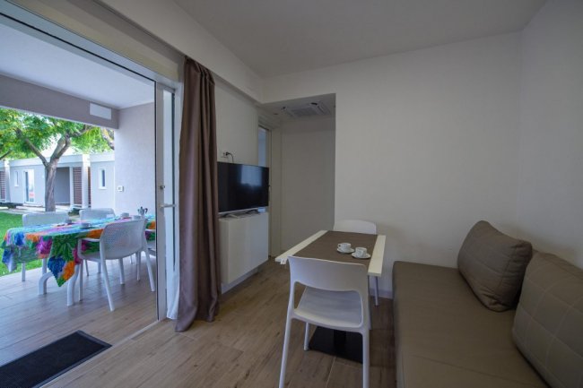 Soggiorno con divano, tavolo e TV. Vista su terrazza esterna.