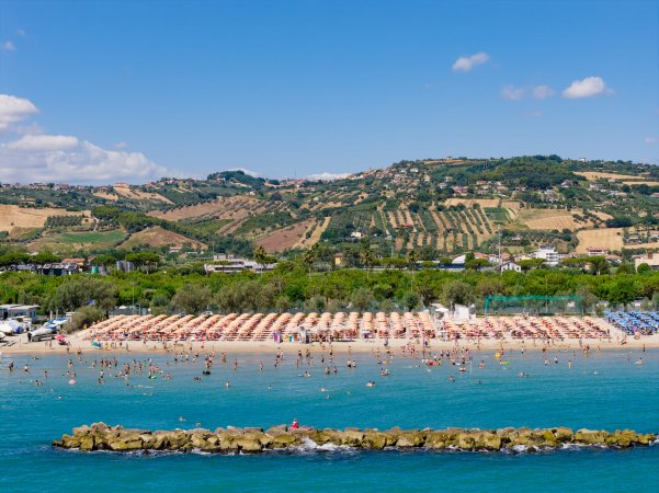 Spiaggia affollata con ombrelloni, mare e colline sullo sfondo.