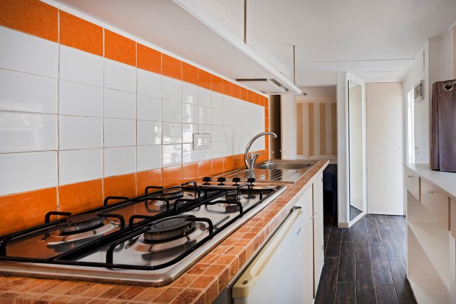 Cucina moderna con piastrelle arancioni e piano cottura a gas.