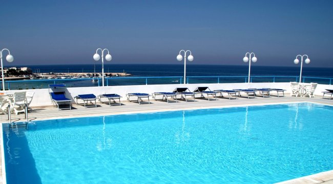 Piscina all'aperto con lettini, lampioni e vista sul mare.