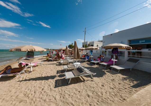 Spiaggia con lettini, ombrelloni beige e persone che prendono il sole vicino al mare.