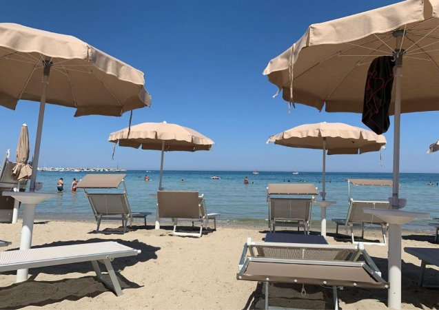 Ombrelloni beige e lettini su una spiaggia sabbiosa con mare calmo sullo sfondo.