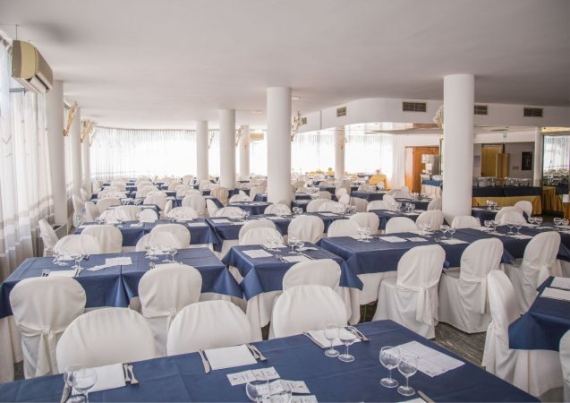 Sala da pranzo con tavoli apparecchiati e sedie bianche.