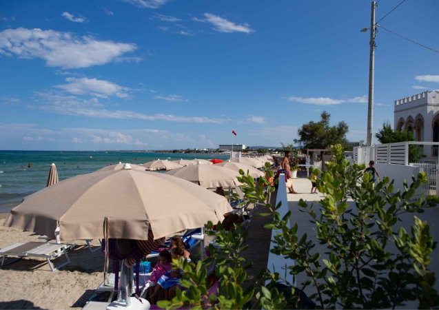 Ombrelloni beige su una spiaggia sabbiosa accanto al mare, con cielo azzurro e nuvole.