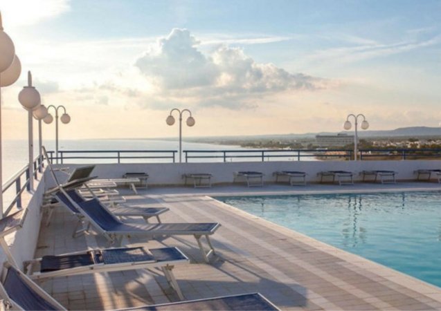 Piscina sul tetto con lettini blu e vista panoramica sul mare al tramonto.