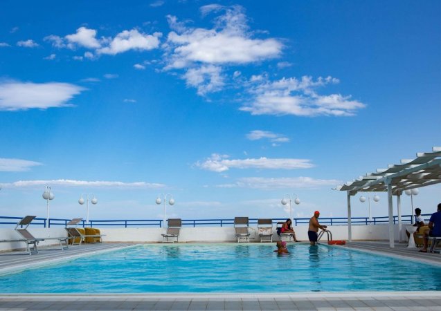 Piscina all'aperto con persone, cielo blu e nuvole bianche, cerchi di luce.